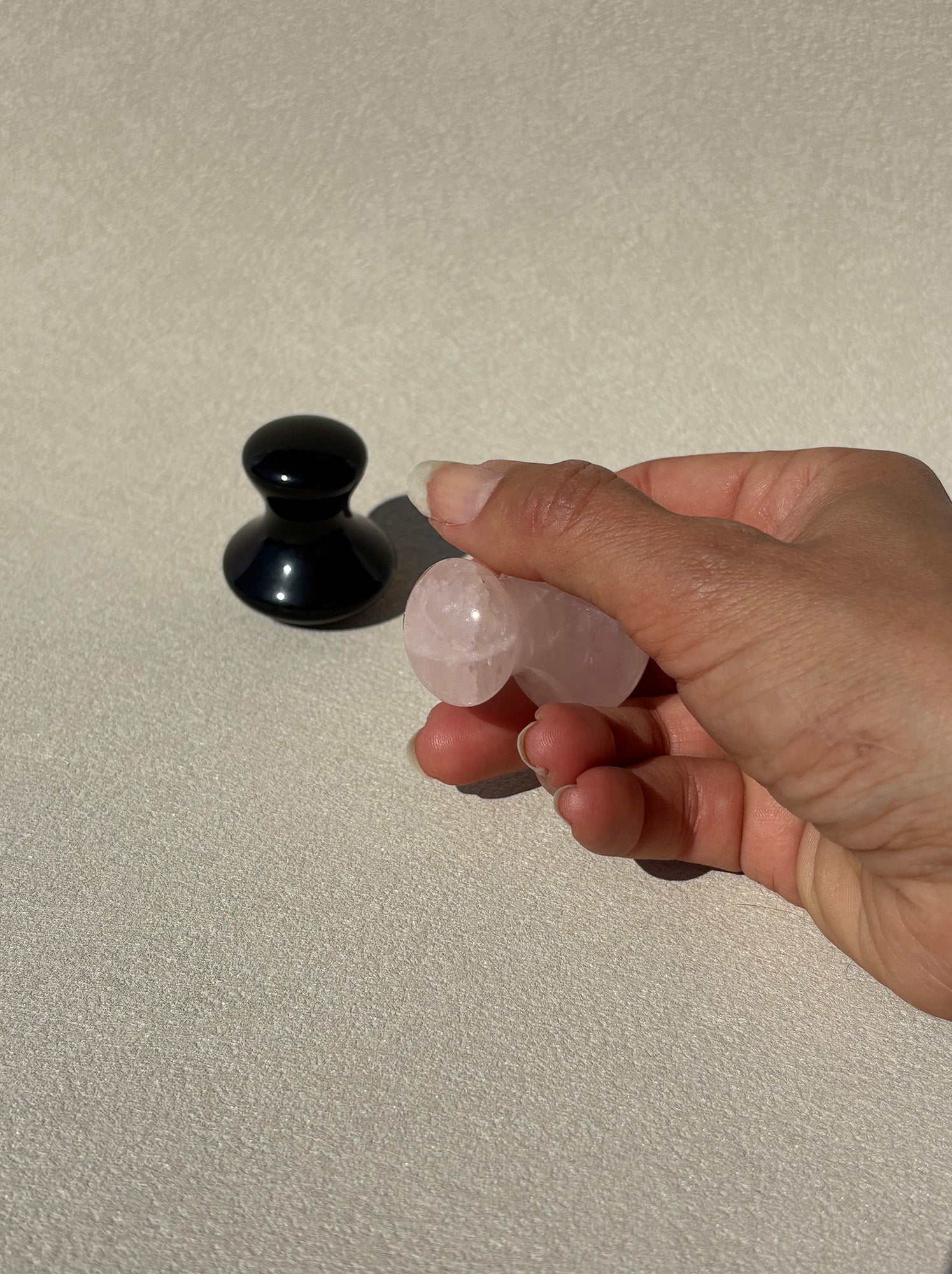 Eine Hand hält den rosafarbenen Gua Sha Stein in Pilzform in einem möglichen Anwendung.