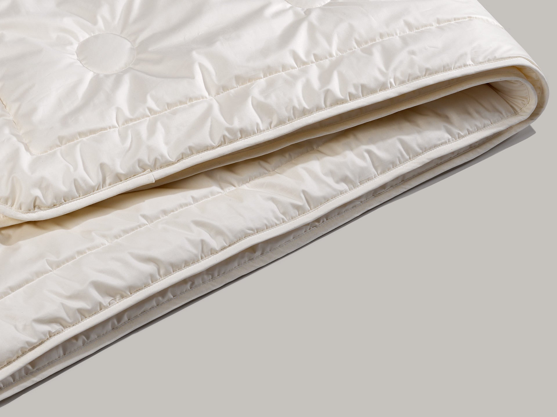 Das Maisfaserduvet welches zusammengelegt ist, mit dem runden Steppmuster im Detail. Die Kanten des Duvets sind mit einem Band versäubert.