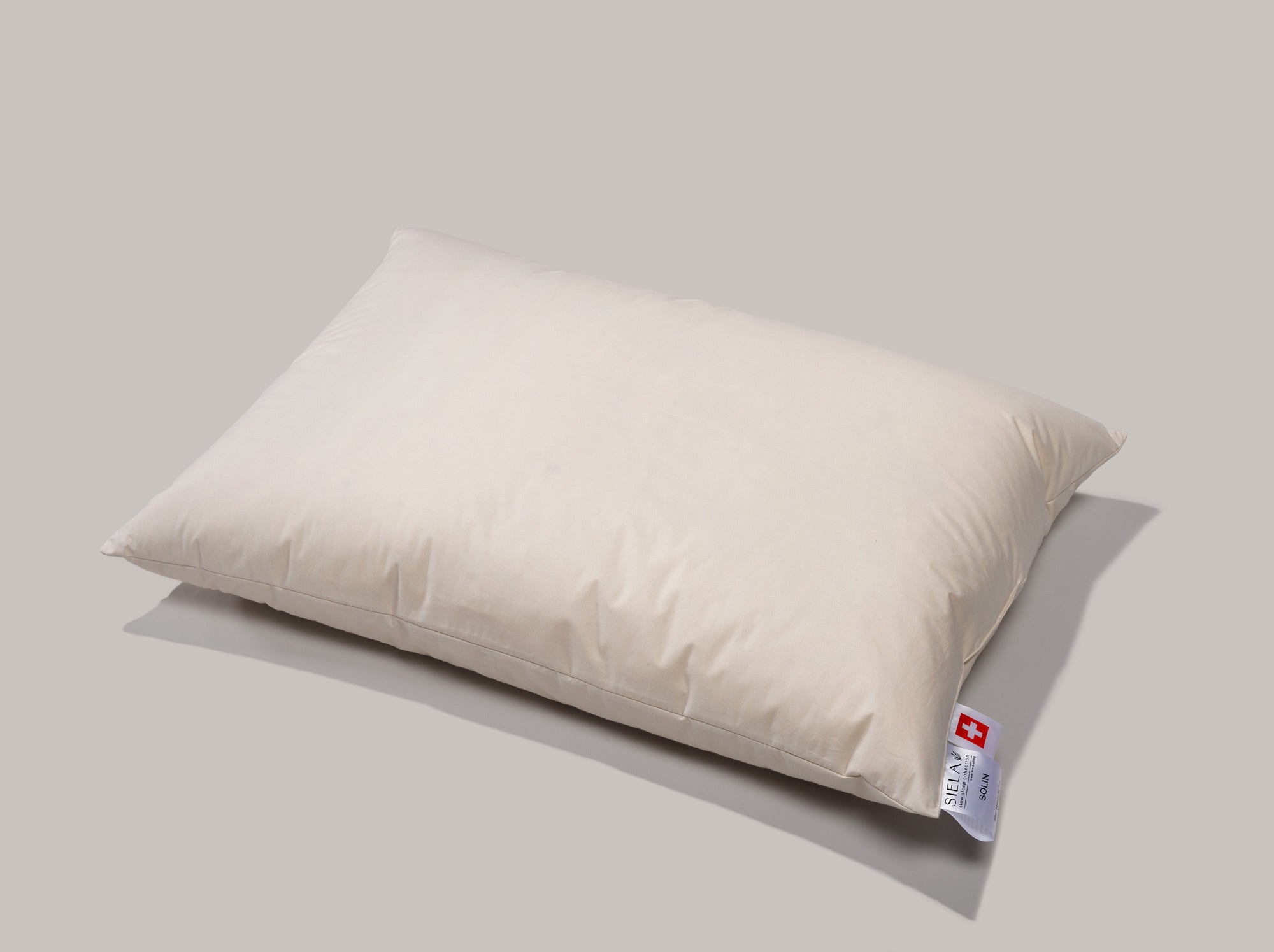 Das Zweikammerkissen Solin liegt auf einer grauen matten Oberfläche. Das Kissen ist beige und etwas angeschrägt hingelegt.
